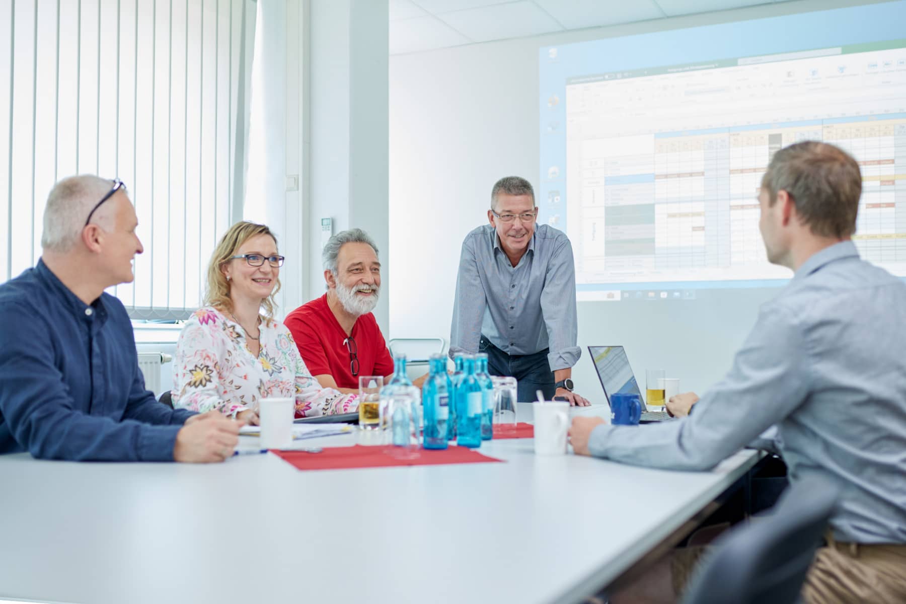 Mehrere Mitarbeiterinnen und Mitarbeiter aus verschiedenen Abteilungen diskutieren an einem Tisch über das kommende Projekt.