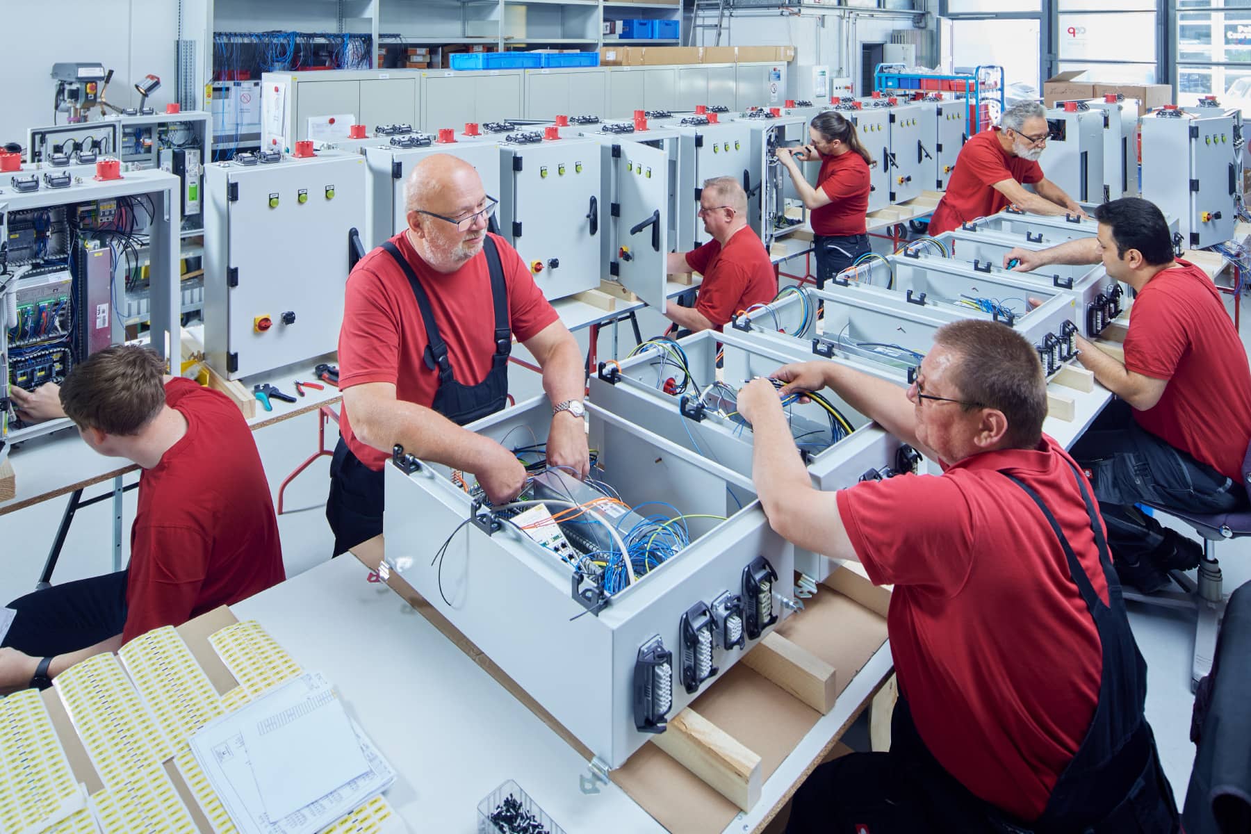 Mehrere Mitarbeiter bauen im Team verschiedene Komponenten in eine Reihe von Schaltschränken ein.