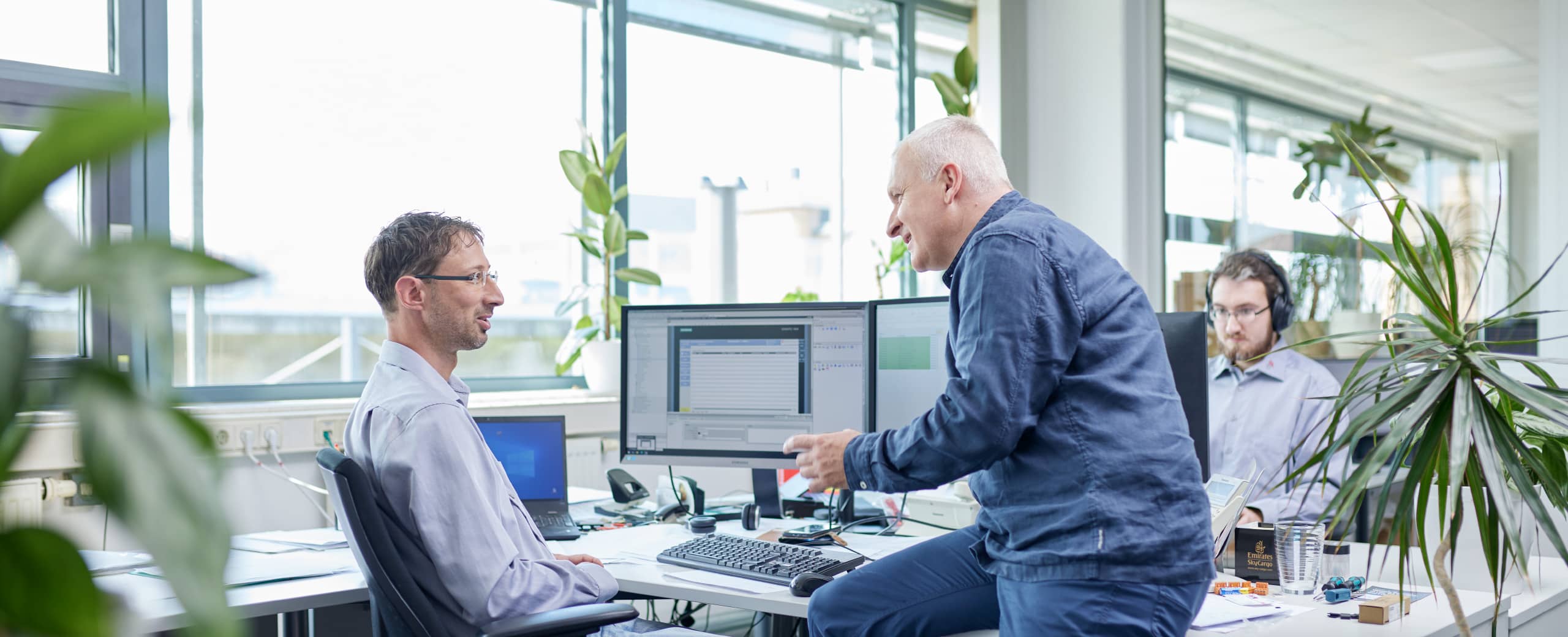 Zwei Mitarbeiter an einem Computerarbeitsplatz diskutieren das kommende Projekt.